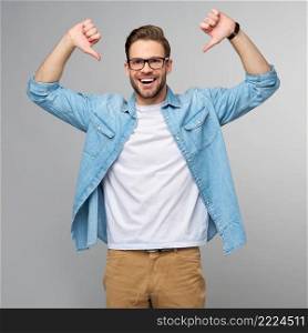 Portrait of young handsome caucasian man in jeans shirt showing at himself by big thumbs standing over light background.. Portrait of young handsome caucasian man in jeans shirt showing at himself by big thumbs standing over light background
