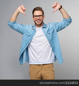 Portrait of young handsome caucasian man in jeans shirt showing at himself by big thumbs standing over light background.. Portrait of young handsome caucasian man in jeans shirt showing at himself by big thumbs standing over light background