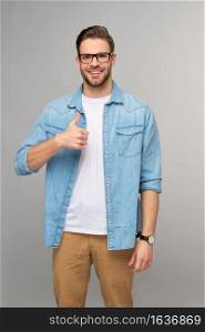 Portrait of young handsome caucasian man in jeans shirt showing big thumb up gesture standing over light background.. Portrait of young handsome caucasian man in jeans shirt showing big thumb up gesture standing over light background
