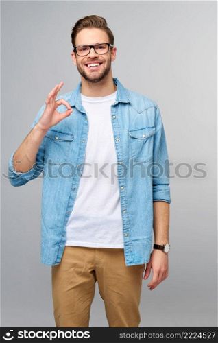 Portrait of young handsome caucasian man in jeans shirt showing ok sign gesture standing over light background.. Portrait of young handsome caucasian man in jeans shirt showing ok sign gesture standing over light background