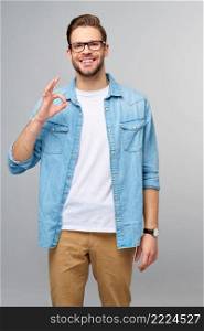Portrait of young handsome caucasian man in jeans shirt showing ok sign gesture standing over light background.. Portrait of young handsome caucasian man in jeans shirt showing ok sign gesture standing over light background