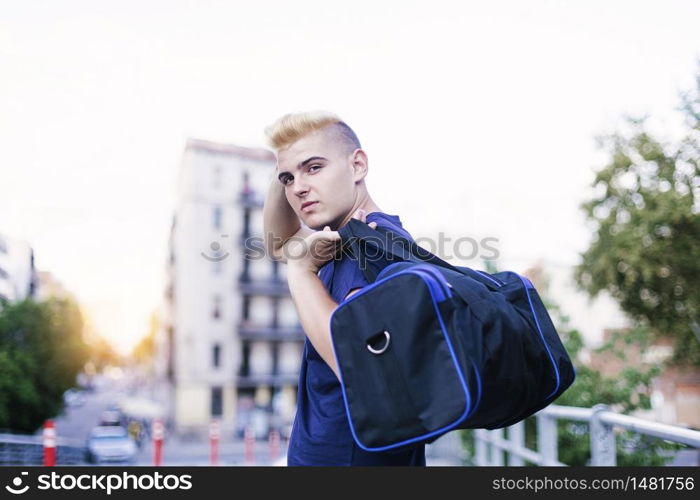 Portrait of young handsome male walking on the street, holding sports bag