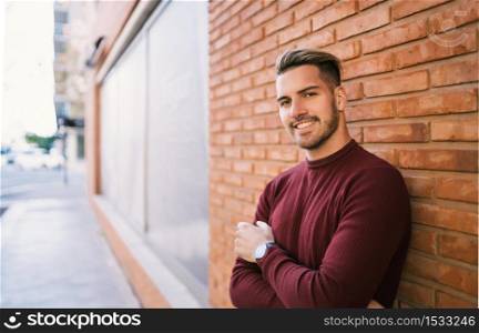 Portrait of young handsome man carrying a backpack and wearing casual clothes against the brick wall in the street. Urban concept.