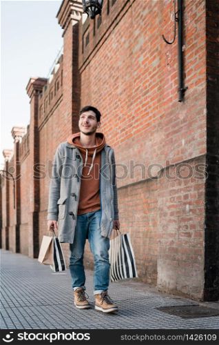 Portrait of young handsome man holding shopping bags while walking on the street. Urban, shop concept.