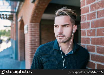 Portrait of young handsome man listening to music with earphones outdoors in the street. Urban concept.