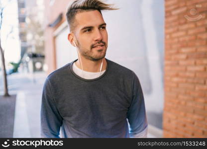 Portrait of young handsome man listening to music with earphones outdoors in the street. Urban concept.