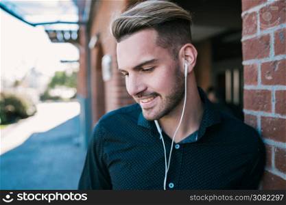 Portrait of young handsome man listening to music with earphones outdoors in the street. Urban concept.