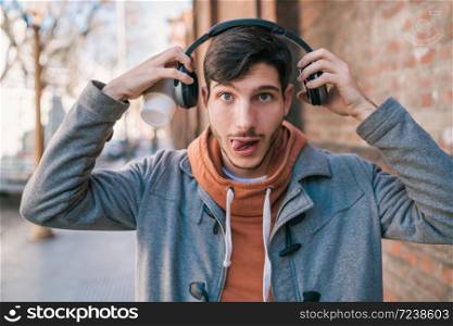 Portrait of young handsome man listening to music with headphones against brick wall. Urban concept.