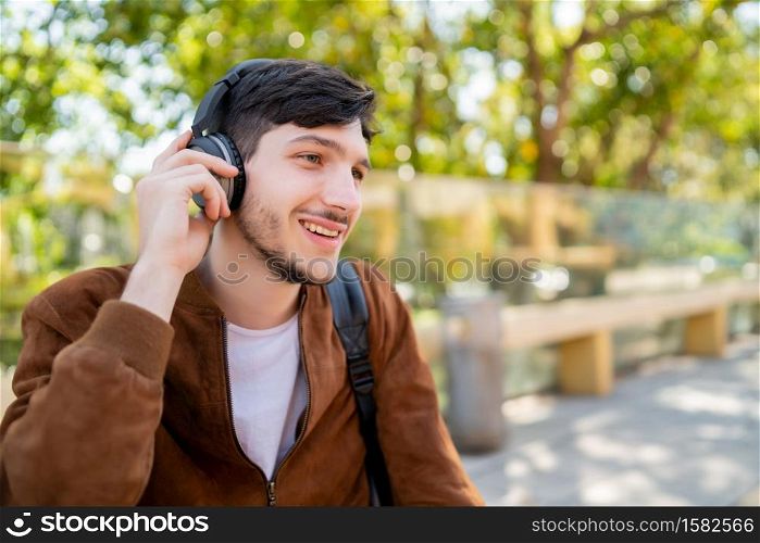 Portrait of young handsome man listening to music with headphones while sitting outdoors. Urban concept.