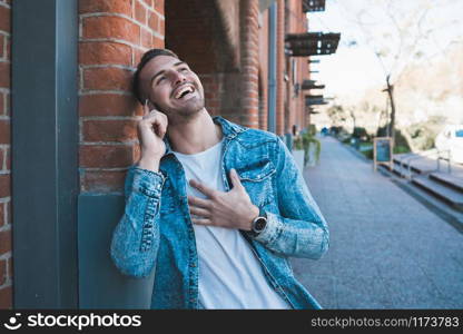 Portrait of young handsome man talking on the phone and laughing outdoors in the street. Communication concept.