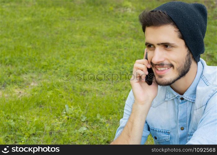 Portrait of young handsome man talking on the phone in a park. Outdoors.