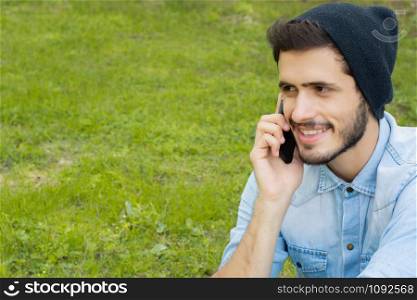 Portrait of young handsome man talking on the phone in a park. Outdoors.