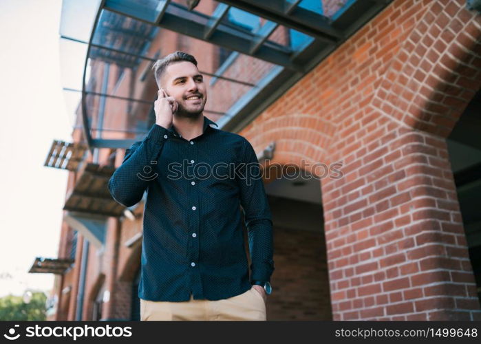 Portrait of young handsome man talking on the phone outdoors in the street. Communication concept.