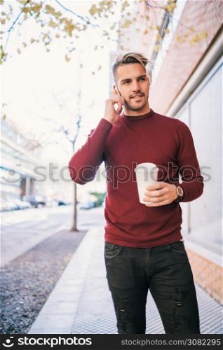 Portrait of young handsome man talking on the phone while holding a cup of coffee outdoors in the street. Communication concept.