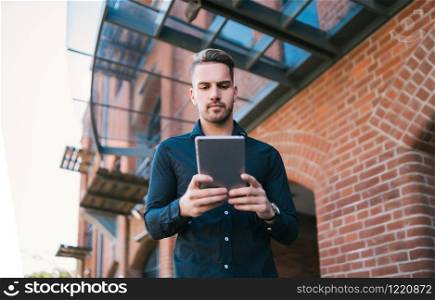 Portrait of young handsome man using his digital tablet outdoors in the street. Technology and urban concept.