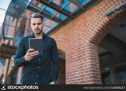 Portrait of young handsome man using his digital tablet outdoors in the street. Technology and urban concept.