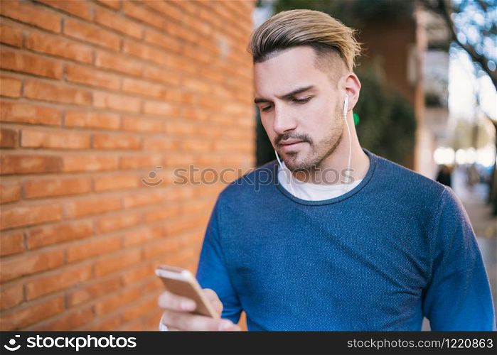 Portrait of young handsome man using his mobile phone with earphones outdoors in the street. Communication concept.