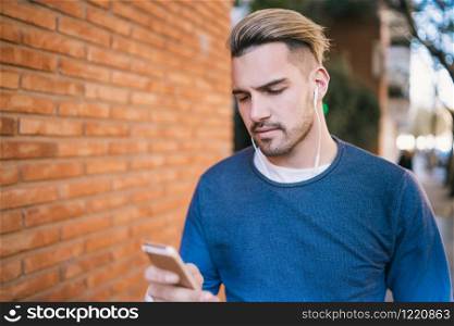 Portrait of young handsome man using his mobile phone with earphones outdoors in the street. Communication concept.