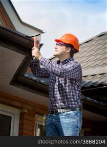 Portrait of young handyman repairing house roof with nails and hammer