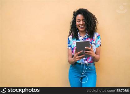 Portrait of young happy afro american latin woman listening music on her digital tablet. Technology concept.