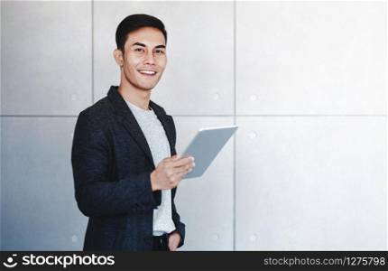 Portrait of Young Happy Businessman Using Digital Tablet. Standing by the Industrial Concrete Wall. Looking at Camera and Smiling