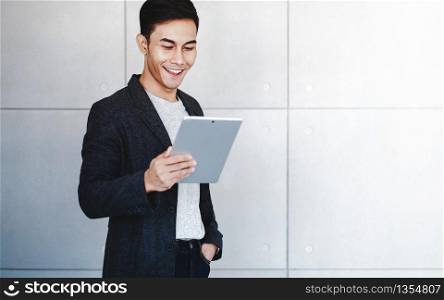 Portrait of Young Happy Businessman Using Digital Tablet. Standing by the Industrial Concrete Wall. Reading Data and Smiling