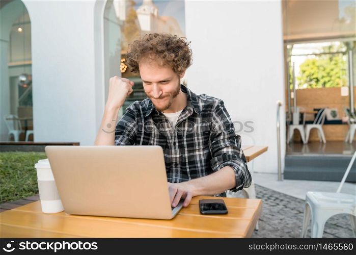Portrait of young happy man looking at laptop and celebrating good news at a coffee shop. Successful concept.