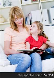 Portrait of young happy mother studing her little daughter to read - at home