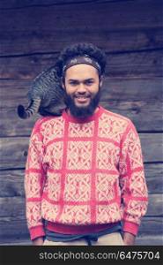 portrait of young hipster man with beard and cat in front of wooden house. portrait of man and cat