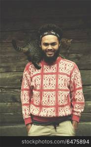 portrait of young hipster man with beard and cat in front of wooden house. portrait of man and cat