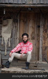 portrait of young hipster, man with beard in front of old vintage wooden house