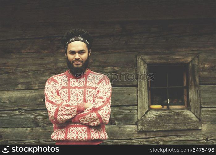 portrait of young hipster, man with beard in front of old vintage wooden house. portrait of young hipster in front of wooden house