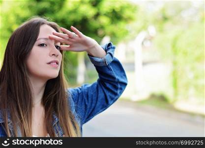 Portrait of young hispanic woman looking far with hand at her forehead, summer outdoors.