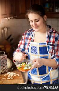Portrait of young housewife preparing salad with cucumbers