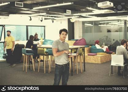 portrait of young indian businessman using laptop computer with his multiethnic business team in background at busy startup office