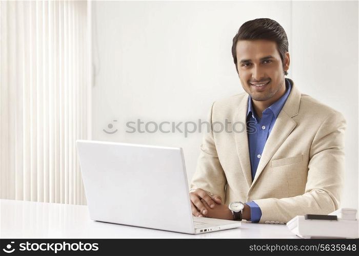 Portrait of young Indian businessman with laptop sitting at office desk