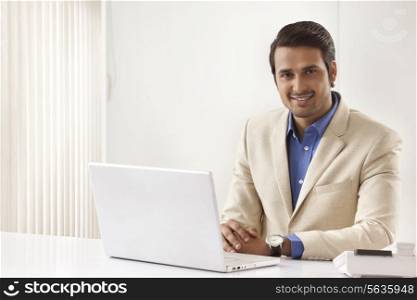 Portrait of young Indian businessman with laptop sitting at office desk