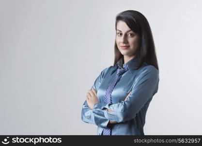 Portrait of young Indian businesswoman with arms crossed standing against gray background