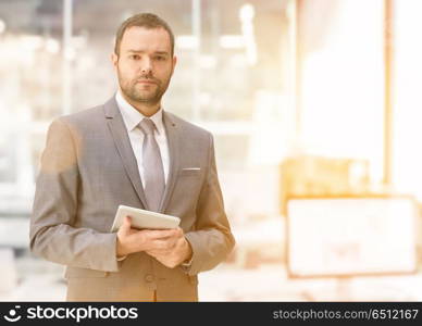 Portrait of young junior businessman using tablet in front of his big modern office. Young businessman in his office