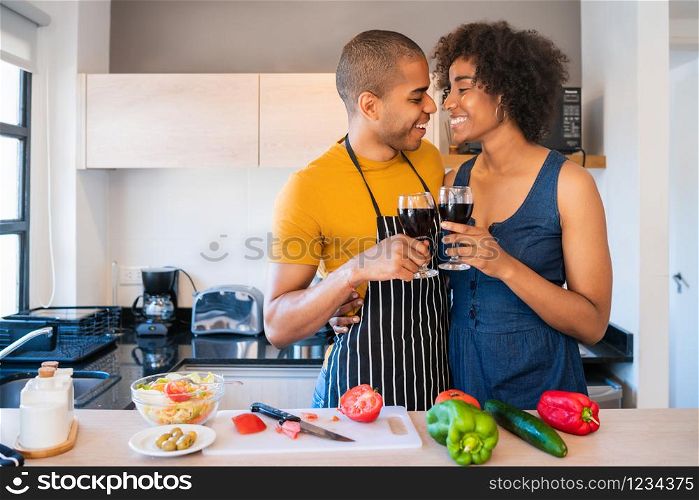 Portrait of young latin couple drinking a glass of wine while cooking together in the kitchen at home. Relationship, cook and lifestyle concept.