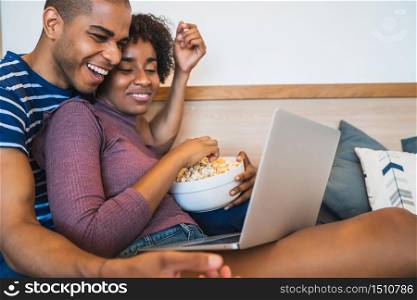 Portrait of young latin couple relaxing and watching a movie with laptop on couch at home. Technology and lifestyle concept.
