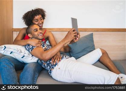 Portrait of young latin couple taking a selfie with digital tablet at home. Technology and lifestyle concept.
