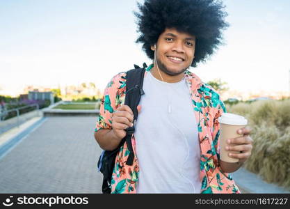 Portrait of young latin man holding a cup of coffee while walking outdoors on the street. Urban concept.