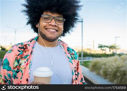 Portrait of young latin man holding a cup of coffee while walking outdoors on the street. Urban concept.
