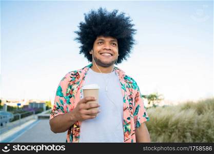 Portrait of young latin man holding a cup of coffee while walking outdoors on the street. Urban concept.