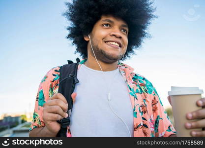 Portrait of young latin man holding a cup of coffee while walking outdoors on the street. Urban concept.