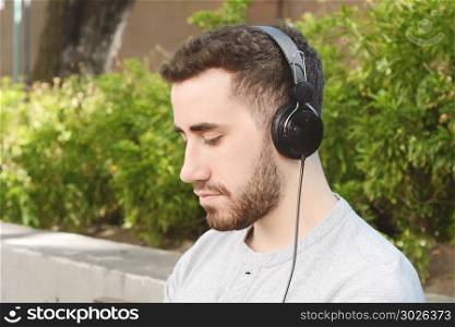 Portrait of young latin man listening to music with black headphones. Outdoors.. Man listening to music.