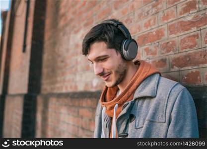 Portrait of young latin man listening to music with headphones against brick wall. Urban concept.