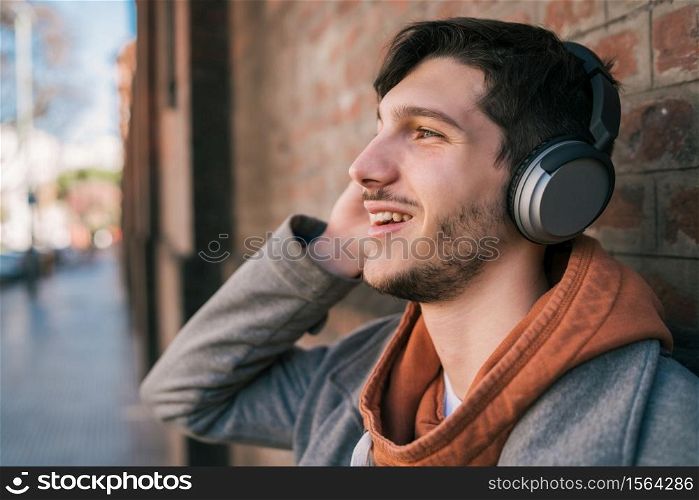 Portrait of young latin man listening to music with headphones against brick wall. Urban concept.