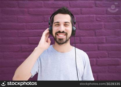 Portrait of young latin man listening to music with headphones. Outdoors.. Latin man listening music with headphones.